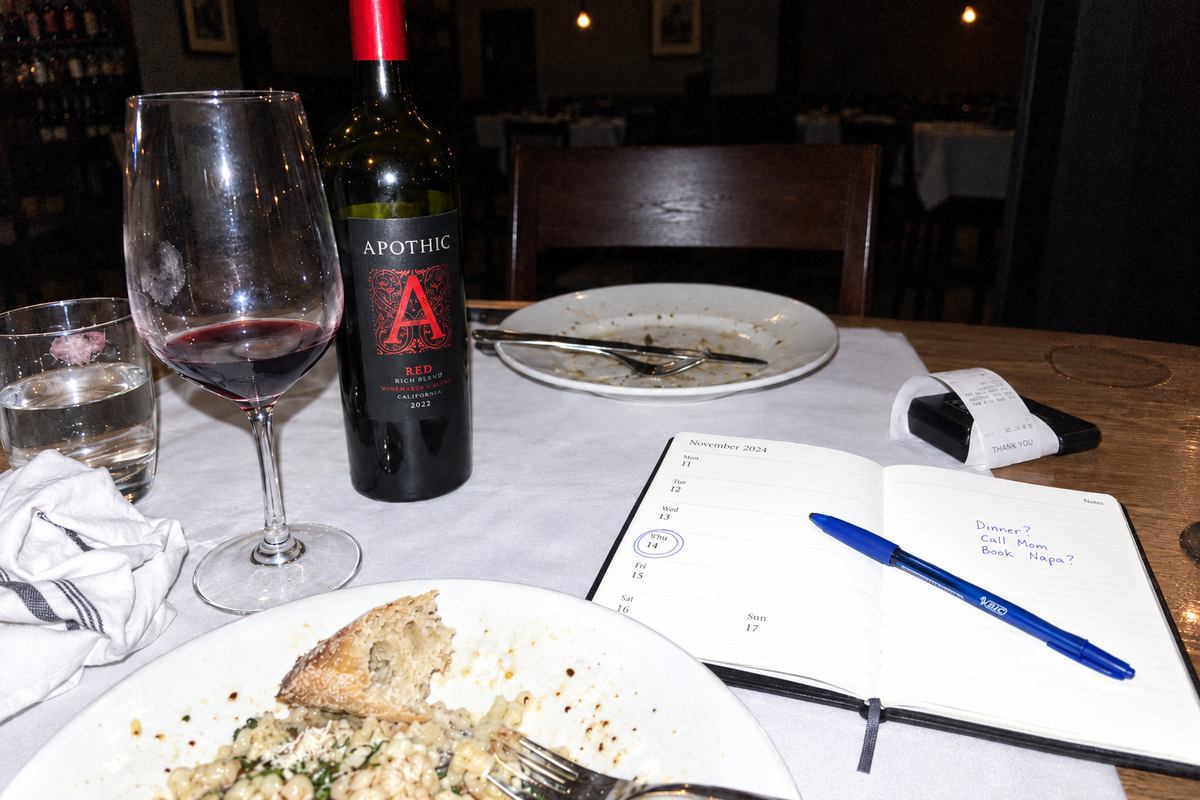 The end of dinner for two: her plate nearly finished, his cutlery laid together, his chair empty, an open planner beside her glass.